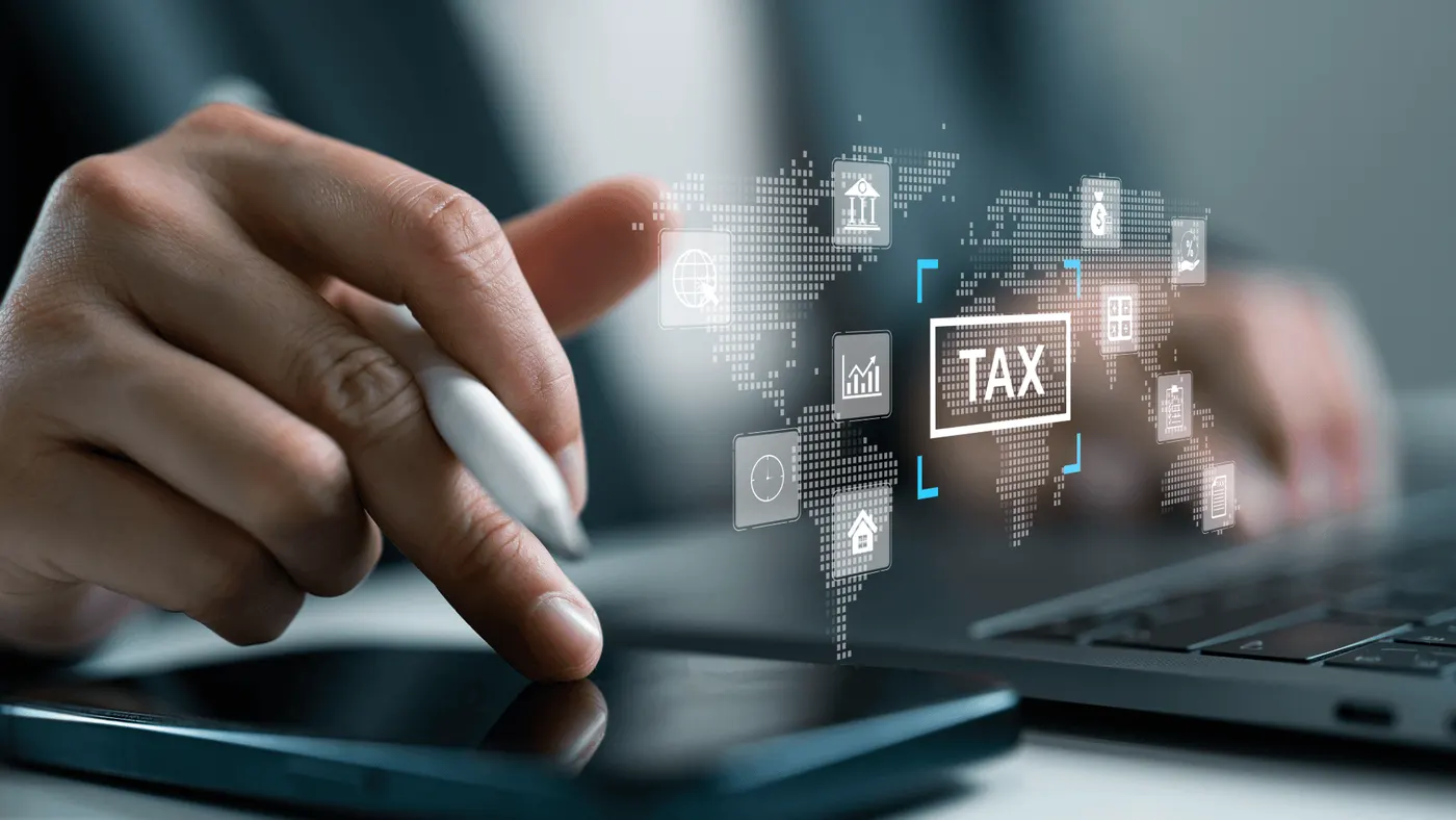 Main tenant un stylet devant une carte du monde et le mot « tax », illustration de la fiscalité internationale
